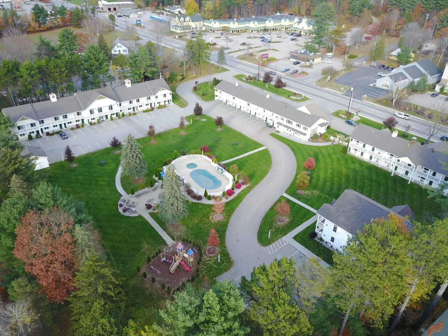 Vista aérea de un complejo hotelero con varias edificaciones, un patio central con piscina y un parque infantil.