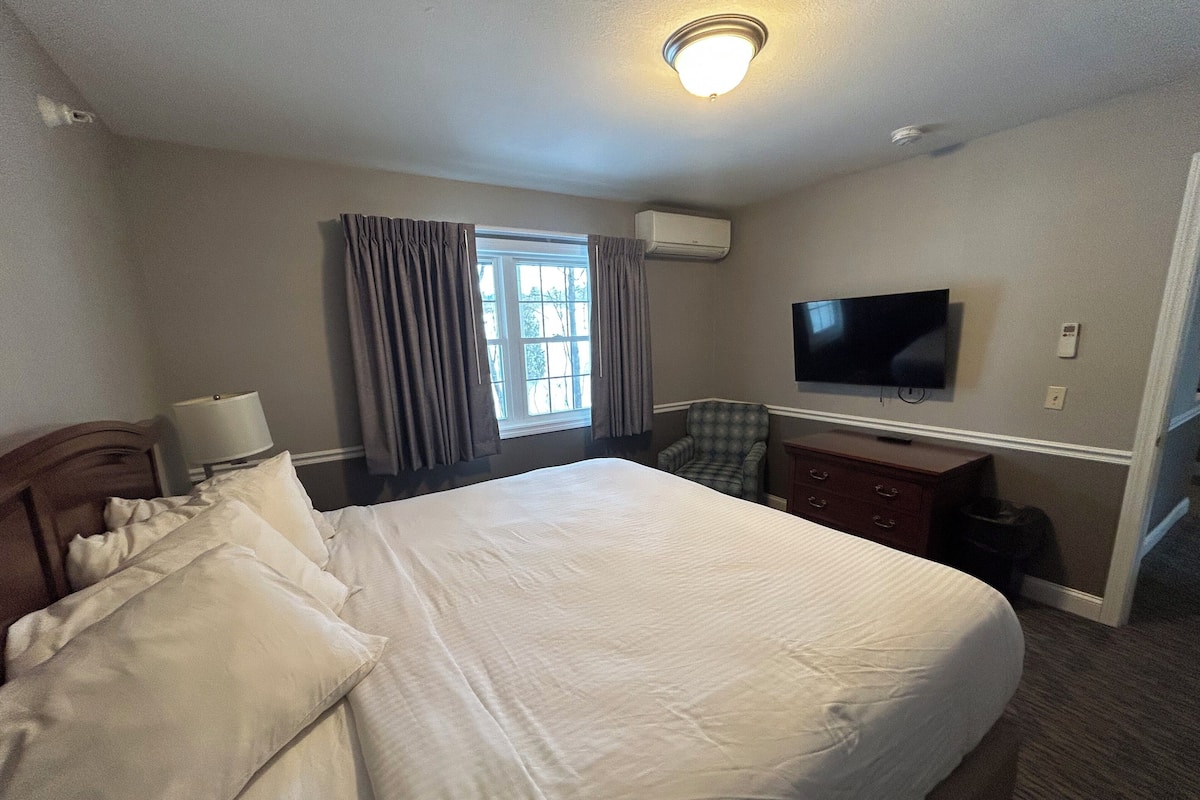 A hotel room with a large bed, a television, a desk, and a window with curtains.