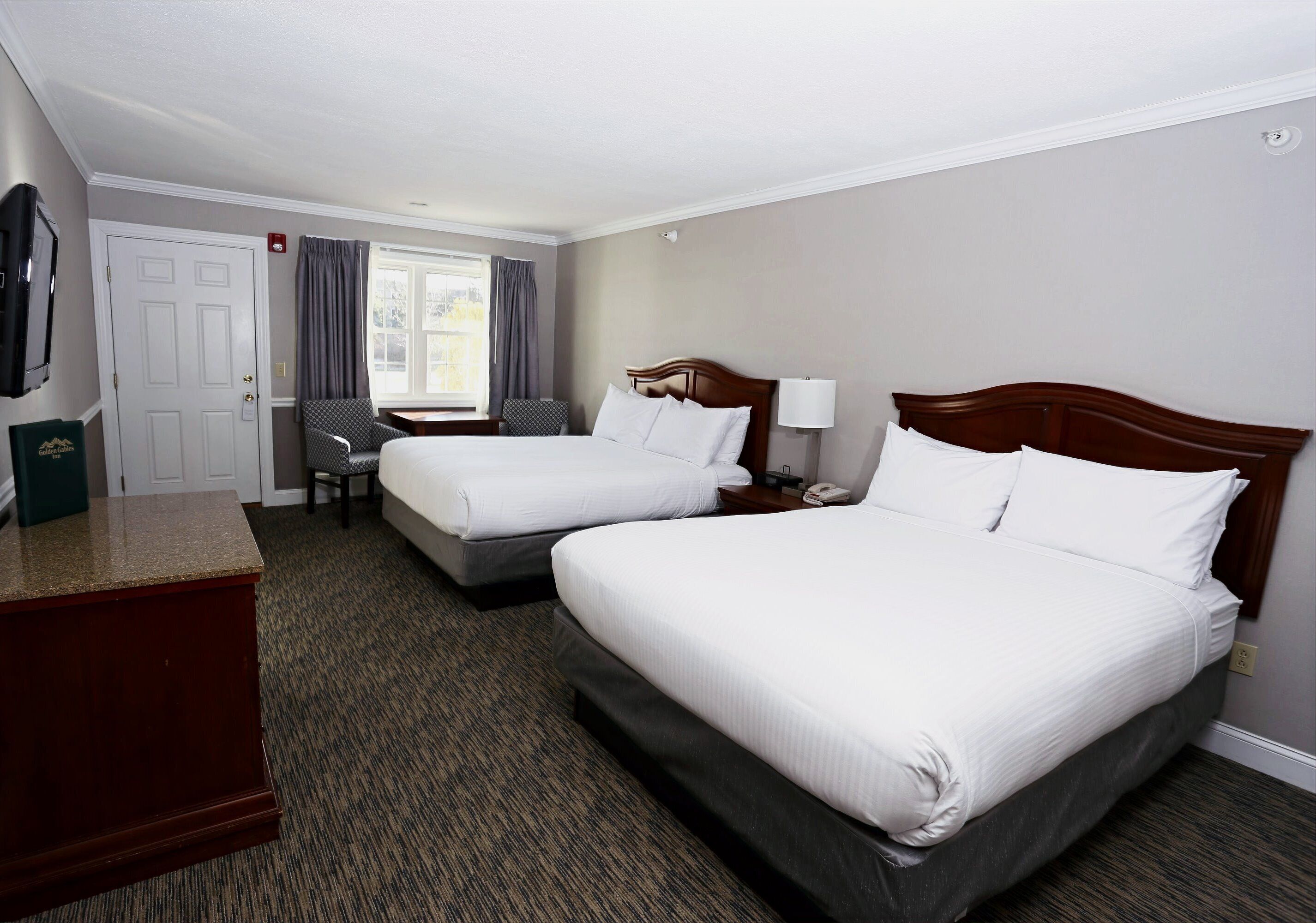 A hotel room with two beds, a desk, a chair, and a television.