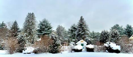 A snow-covered landscape with a small white building surrounded by snow-laden trees and bushes.