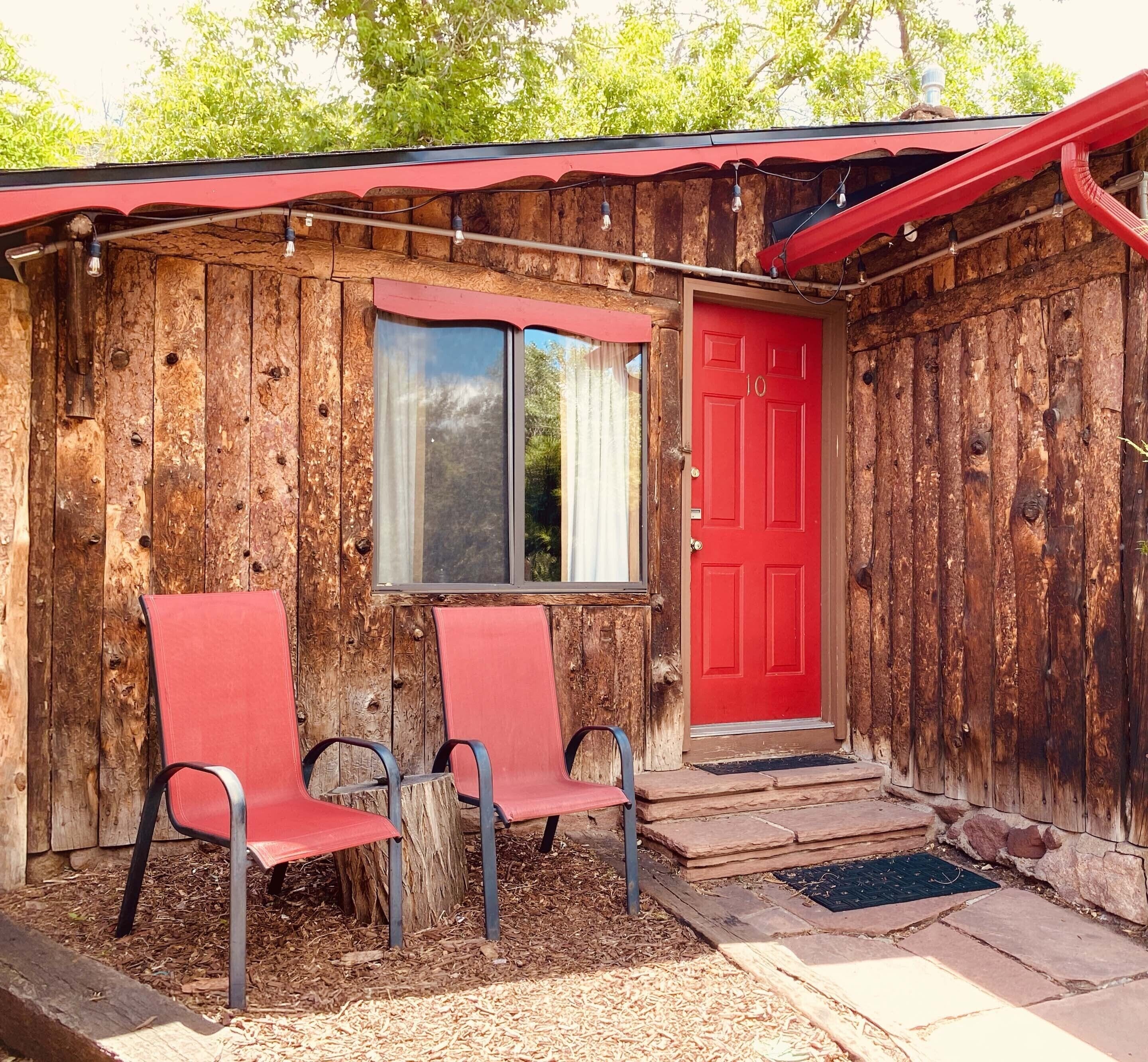 A rustic wooden cabin with a red door and two red chairs outside.