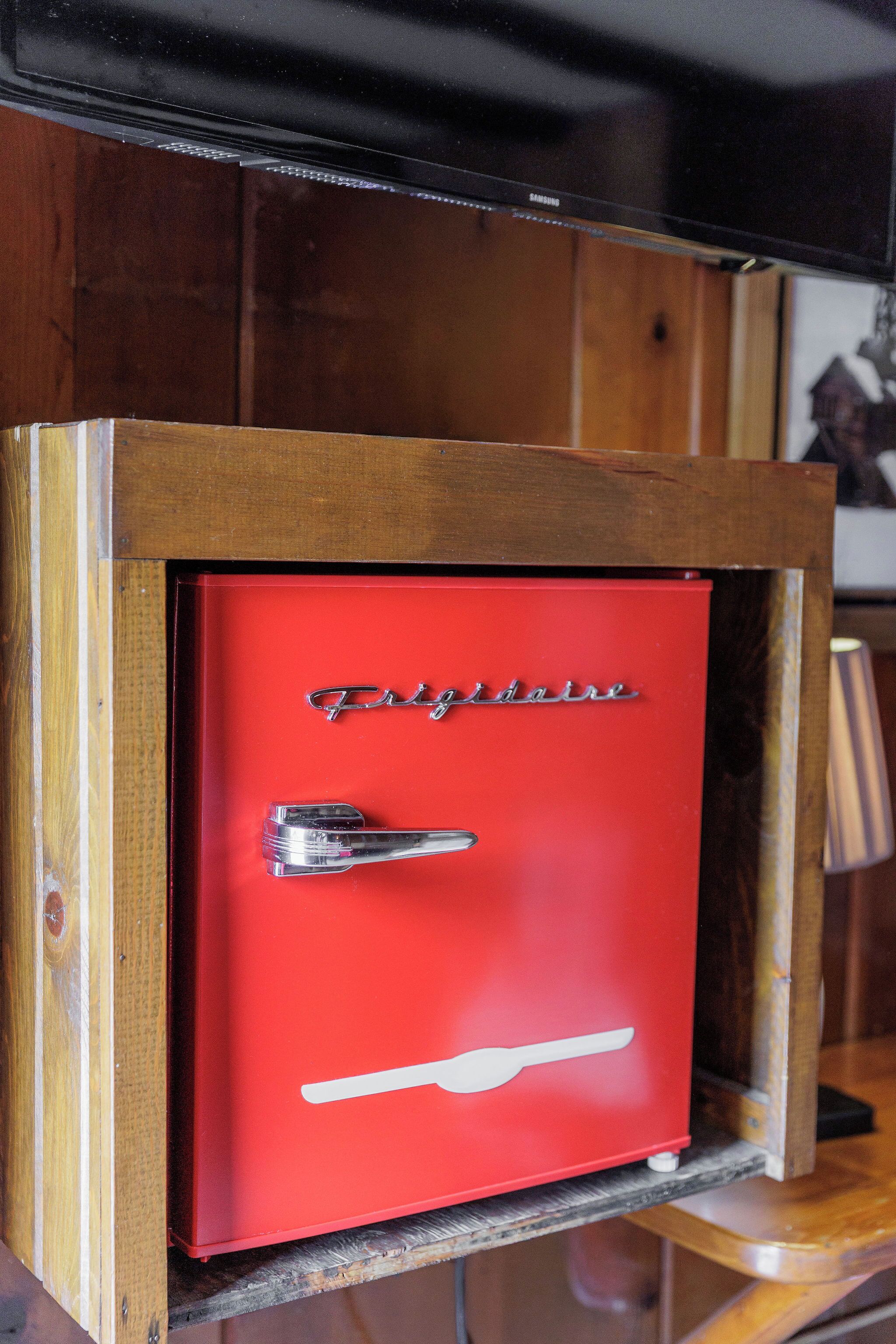 A red safe with a handle and the word 'Frigidaire' on it, placed inside a wooden cabinet.
