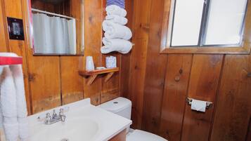 Un bany de fusta amb un lavabo, un vàter i un escorredor de tovalloles amb tovalloles doblegades.