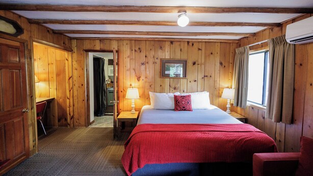 A wooden-paneled room with a bed, two bedside tables with lamps, a door, and a window with curtains. - Foot of the Mountain Motel (Boulder)
