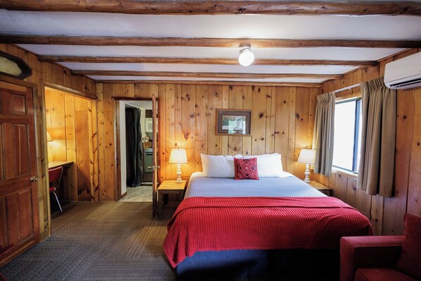 A wooden-paneled room with a bed, two bedside tables with lamps, a door, and a window with curtains. - Foot of the Mountain Motel (Boulder)