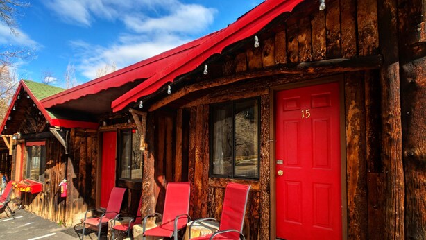 A rustic cabin with a red door marked '15', wooden exterior, and outdoor seating with red chairs. - Foot of the Mountain Motel (Boulder)