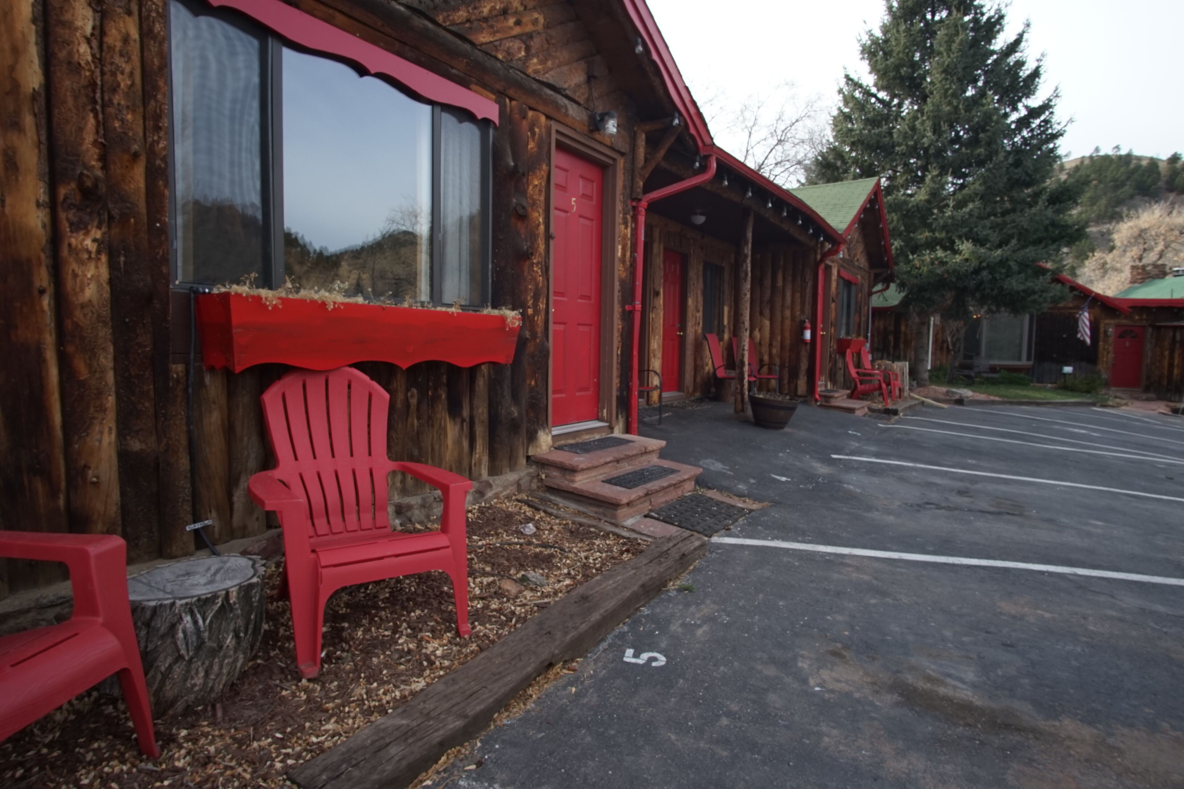 A rustic wooden building with a red door and windows, a red chair outside, and a parking lot with a white line marked '5'.