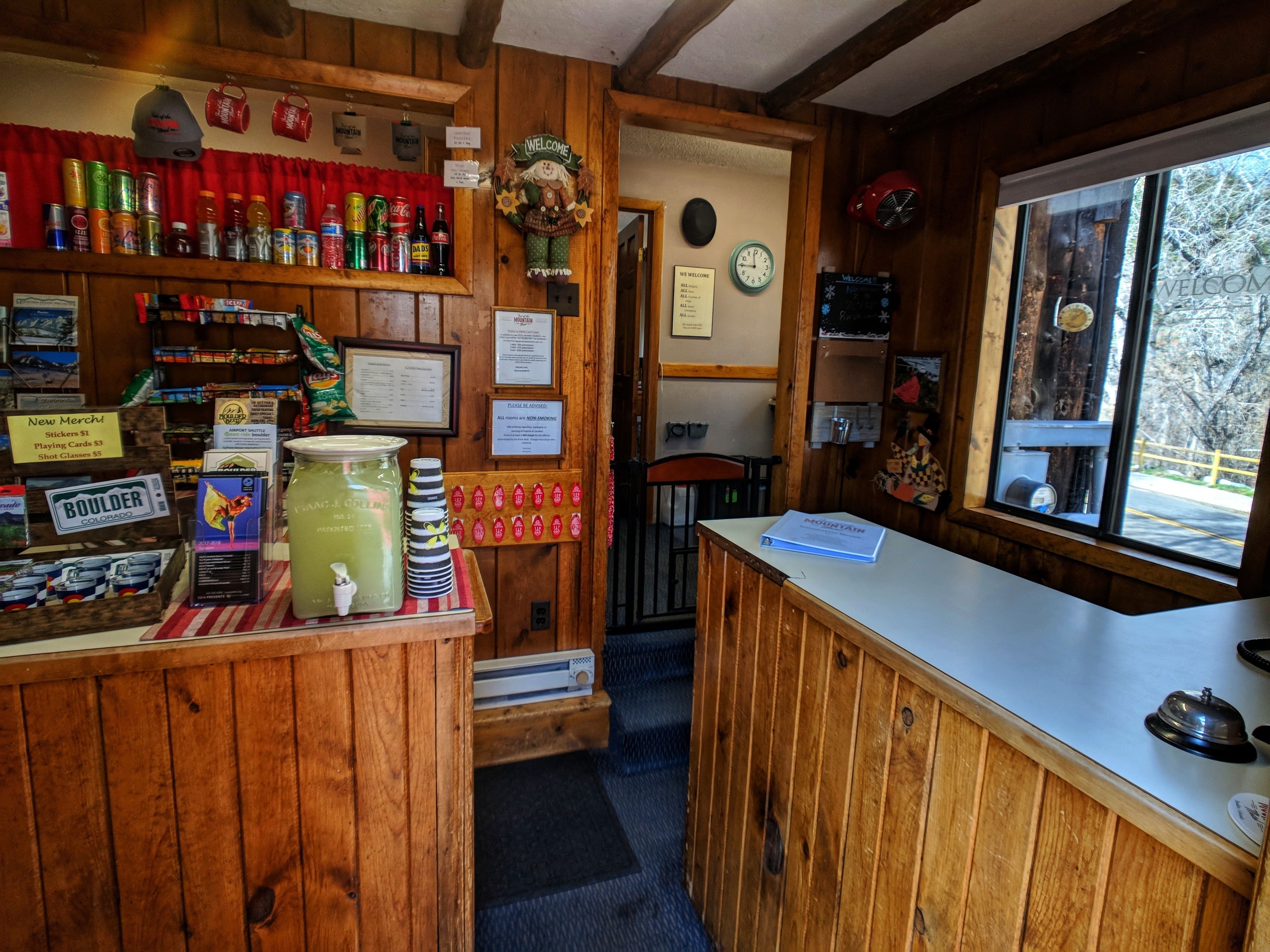A wooden bar area with a rustic decor, including a welcome sign, a clock, and various beverages on shelves.