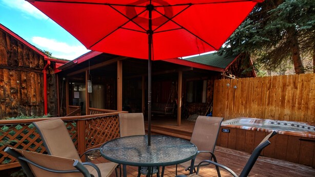 A wooden deck with a round table and chairs, a red umbrella, and a hot tub. - Foot of the Mountain Motel (Boulder)