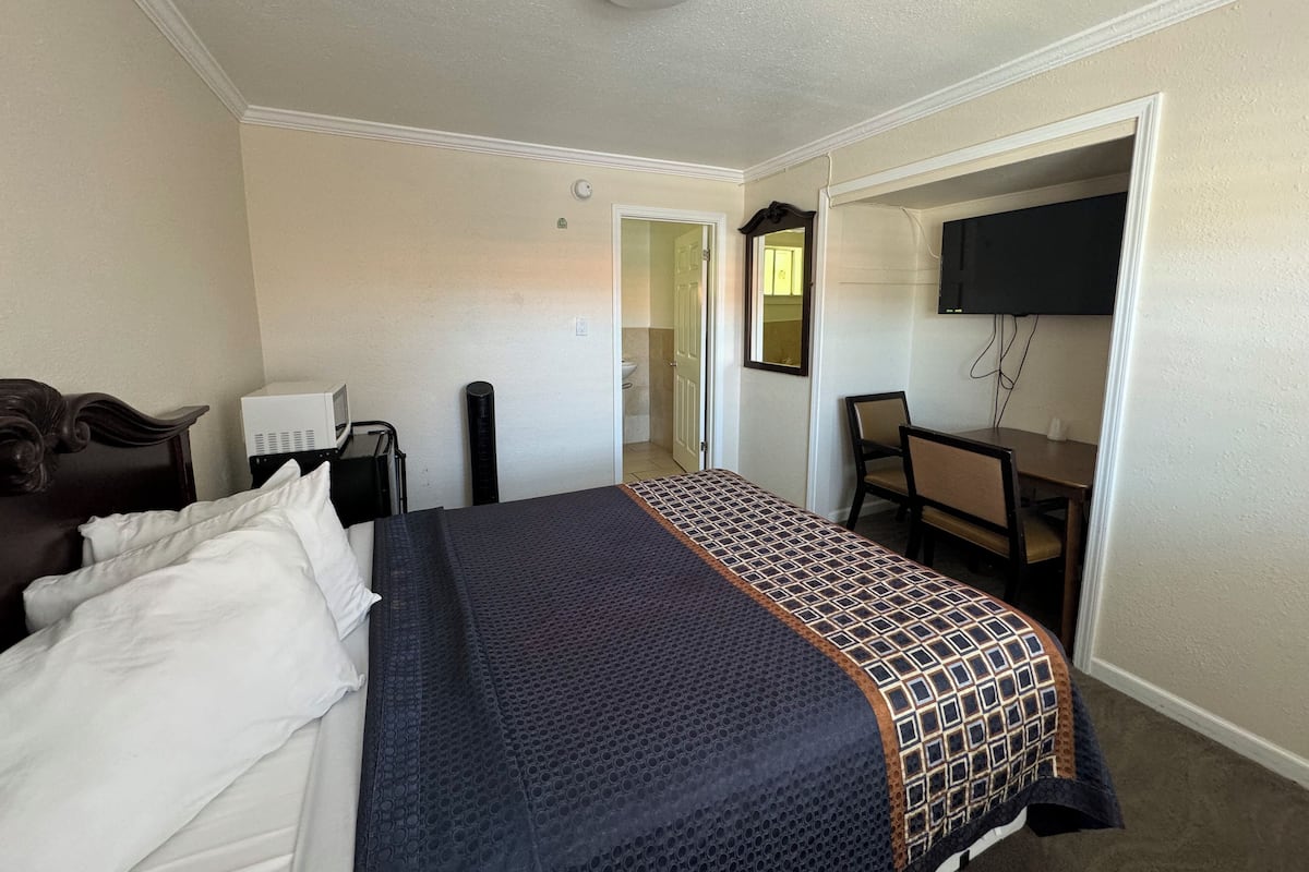 A hotel room with a bed, a desk, a chair, a television, and a door leading to a bathroom.