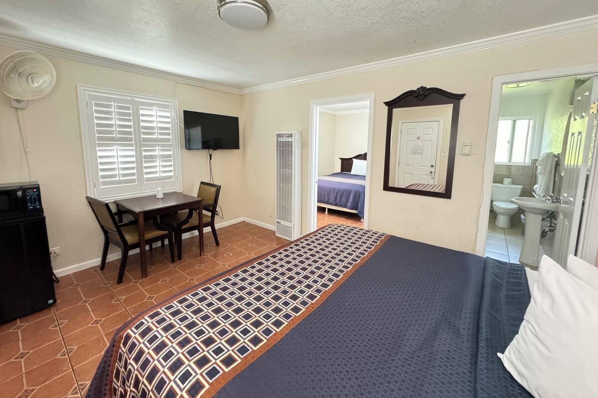 A bedroom with a bed, a desk with a chair, a TV, a heater, and a bathroom visible through an open door.