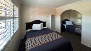 A hotel room with a large bed, a smaller bed, a window with blinds, a ceiling light, and a view of the outside. - Tamalpais Motel (Mill Valley)