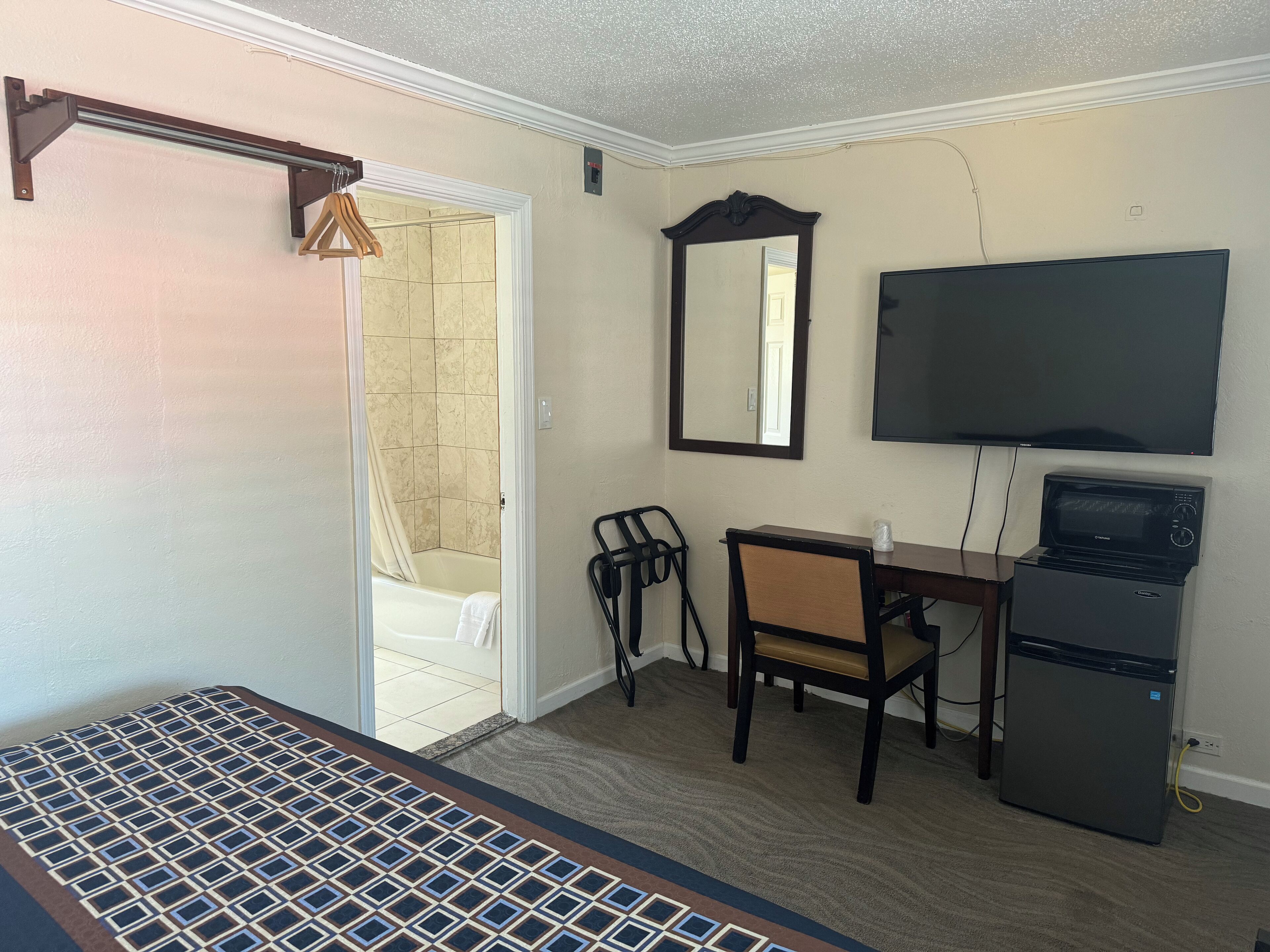 A hotel room with a bed, a desk, a chair, a television, a microwave, and a shower.