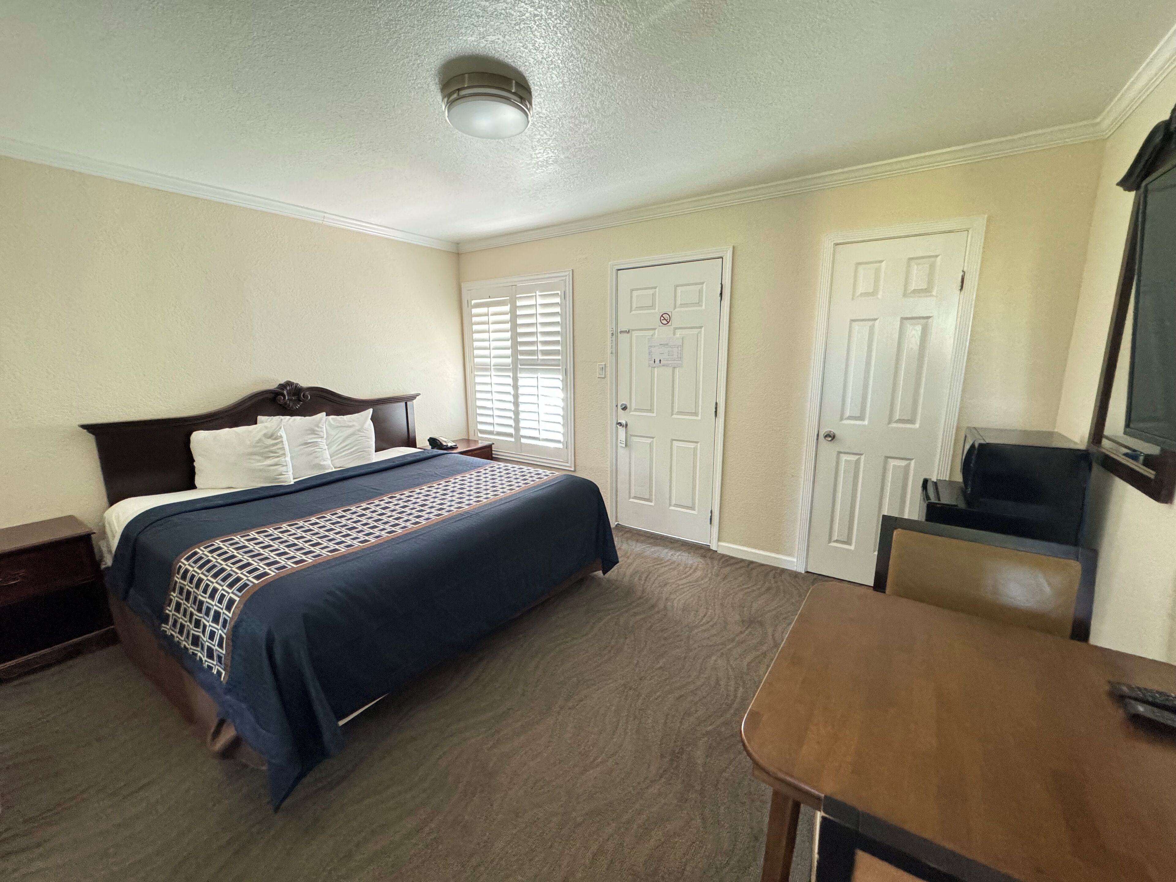 A hotel room with a bed, a desk, a television, and two doors.
