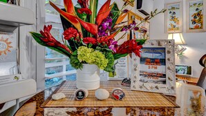 A reception desk with a floral arrangement, framed welcome sign, and a check-in/out schedule. - Island Bay Resort (Tavernier)