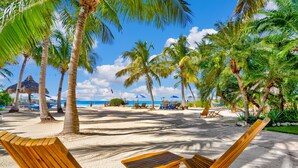A beach with wooden lounge chairs and umbrellas, palm trees, and a clear view of the ocean. - Island Bay Resort (Tavernier)