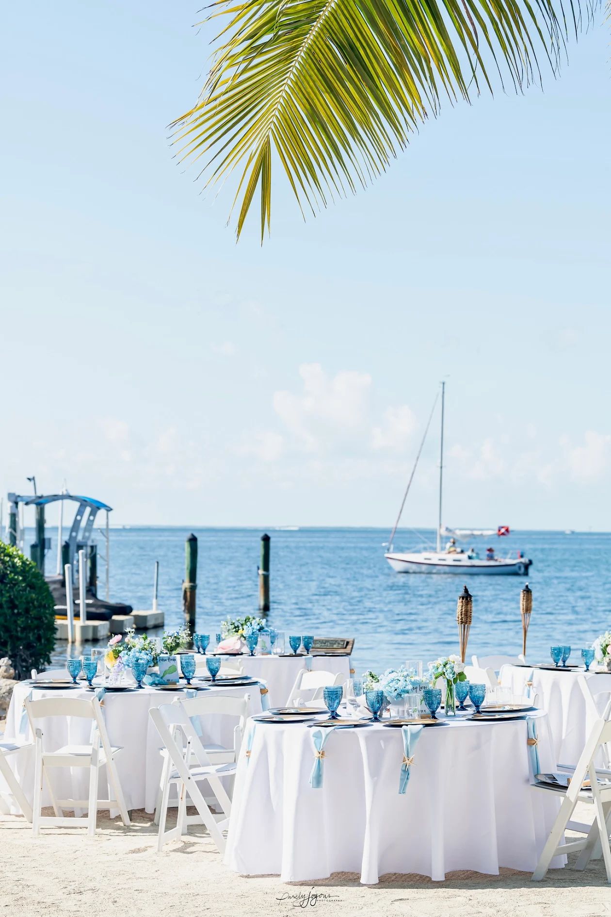 Un espace de restauration en plein air avec des tables et des chaises blanches, le tout mis en valeur par un décor composé d’une mer calme et d’un ciel dégagé.