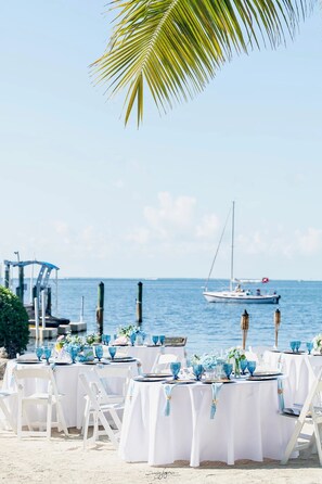 An outdoor dining area with white tables and chairs, set against a backdrop of a calm sea and a clear sky. - Island Bay Resort (Tavernier)