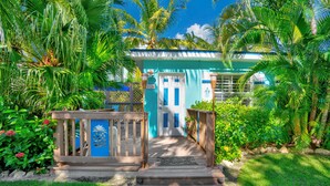 A tropical resort with a wooden deck leading to a blue door, surrounded by lush greenery and palm trees. - Island Bay Resort (Tavernier)