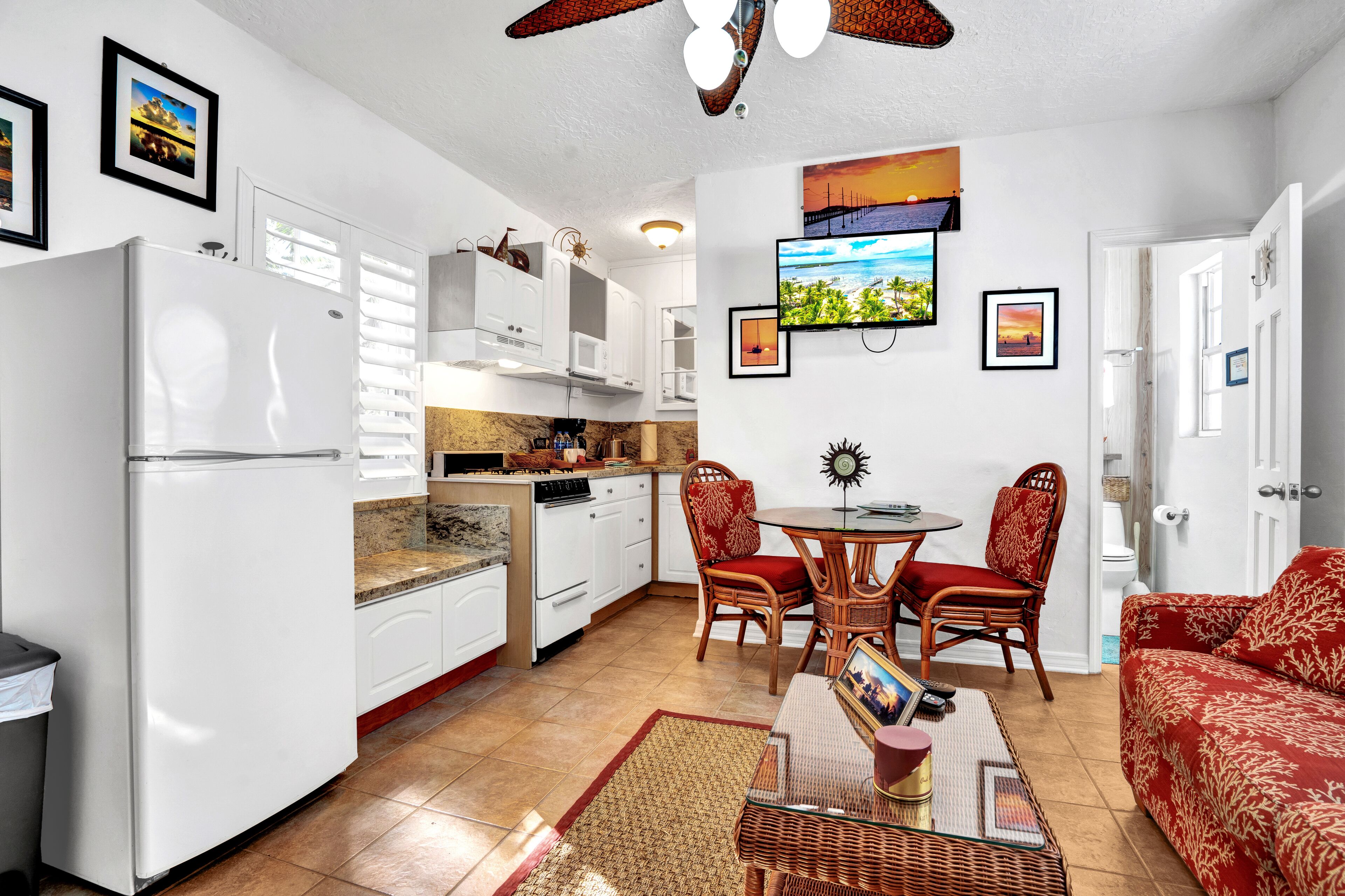 A compact kitchen with white appliances, a dining area with a round table and chairs, and a red sofa.