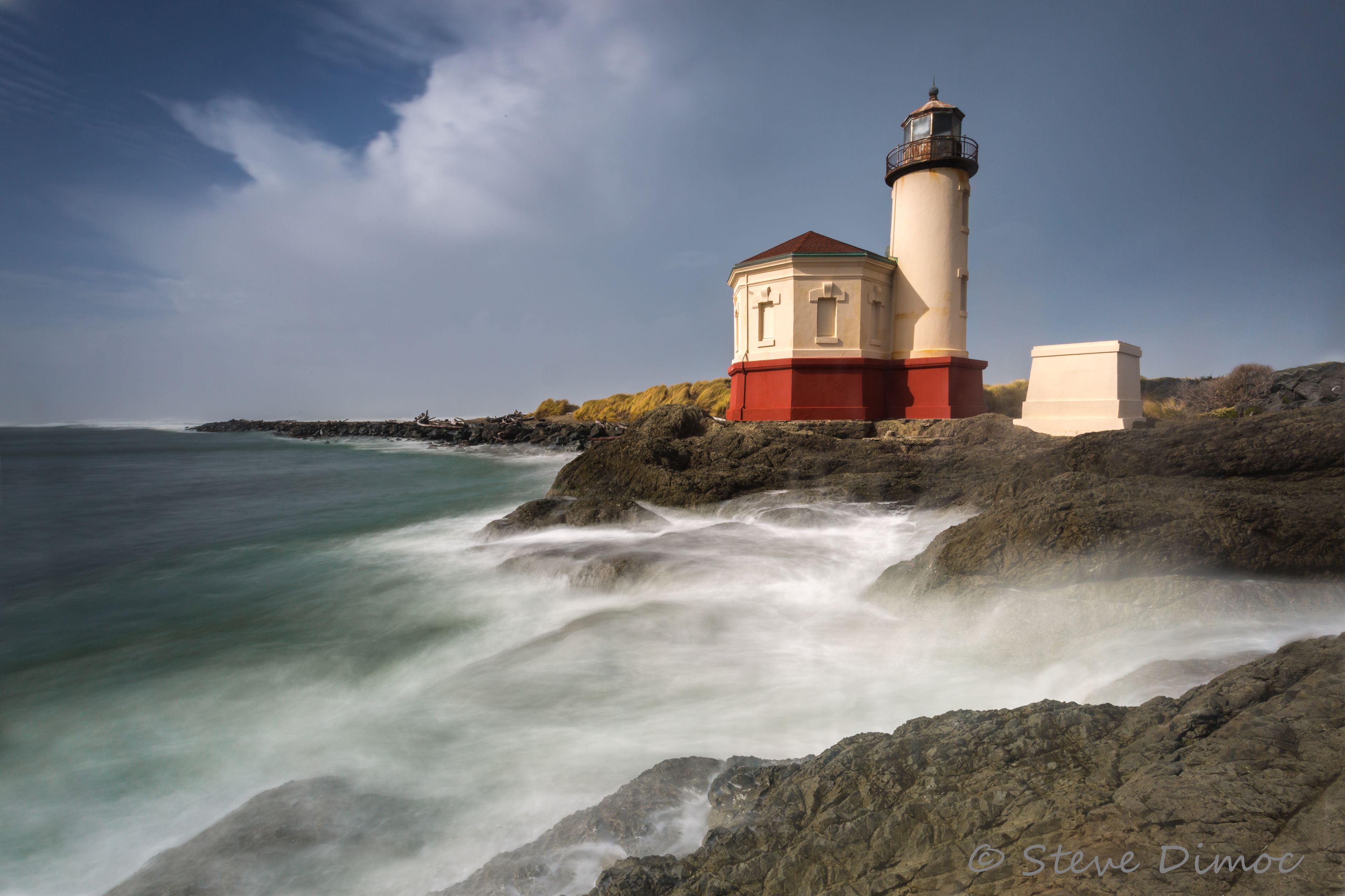 Un phare sur une côte rocheuse, sous un ciel dégagé.