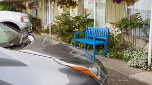 A car parked in front of a building with a porch, a blue bench, and hanging flower baskets. - La Kris Inn (Bandon)