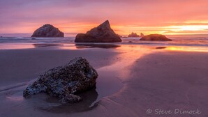 A beach with large rocks and calm water during sunset. - La Kris Inn (Bandon)