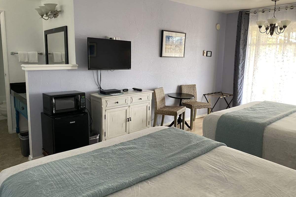 A hotel room with two beds, a television, a desk with a computer, a chair, and a window with curtains.
