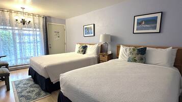 Una camera d'albergo con due letti, una finestra con tende, una lampada e un quadro appeso al muro.