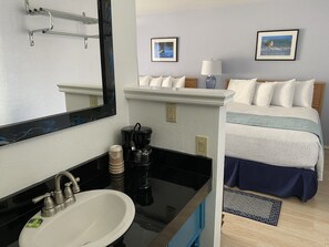A hotel room with a large mirror, a sink, a coffee maker, a bed with a blue and white bedspread, and two framed pictures on the wall. - La Kris Inn (Bandon)