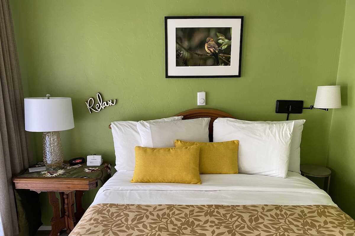 A hotel room with a bed, a nightstand with a lamp, a framed picture on the wall, and a 'Relax' sign.