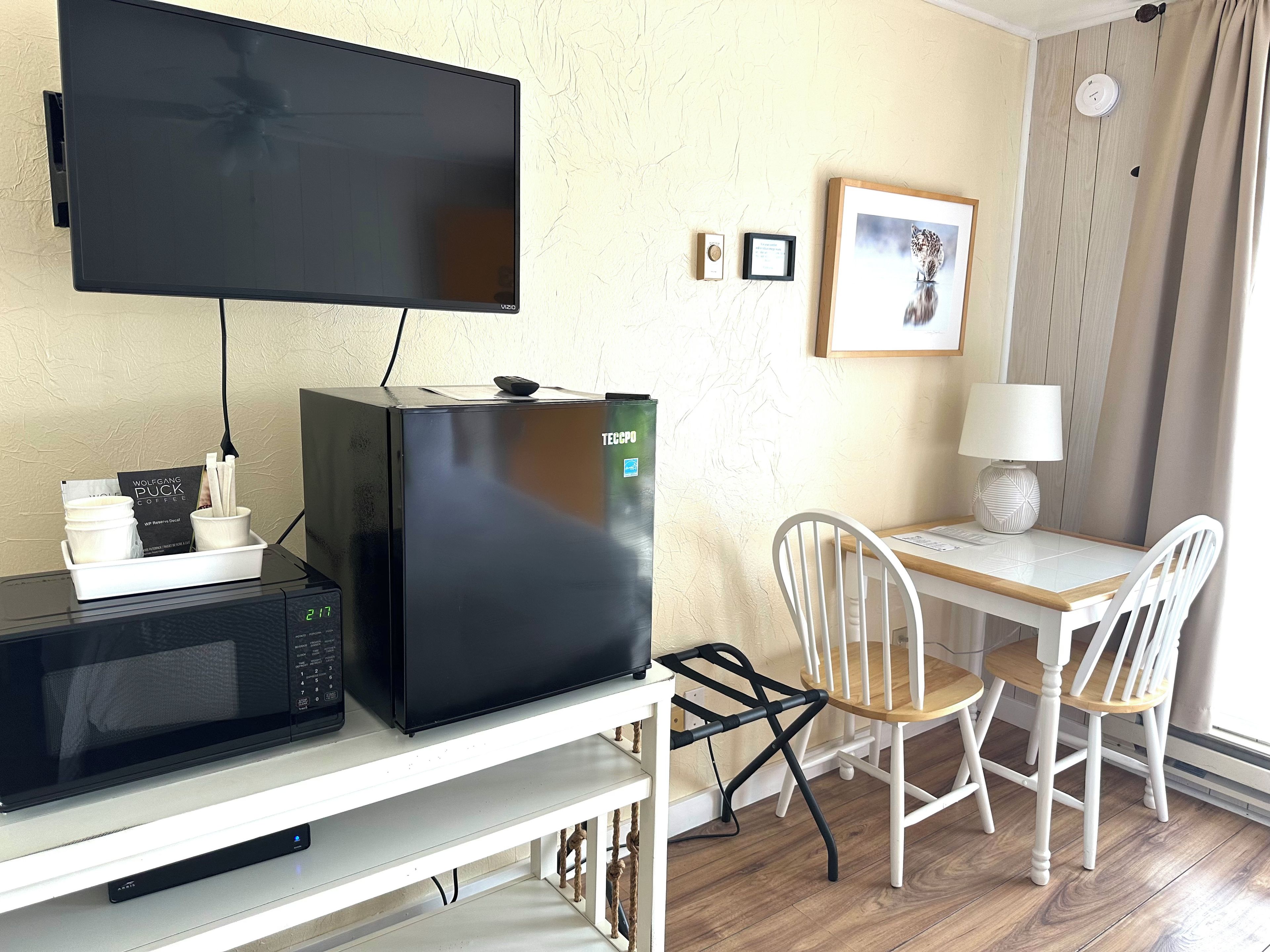 A kitchenette with a microwave, toaster, and coffee maker, a television, a framed picture on the wall, and a table with chairs.