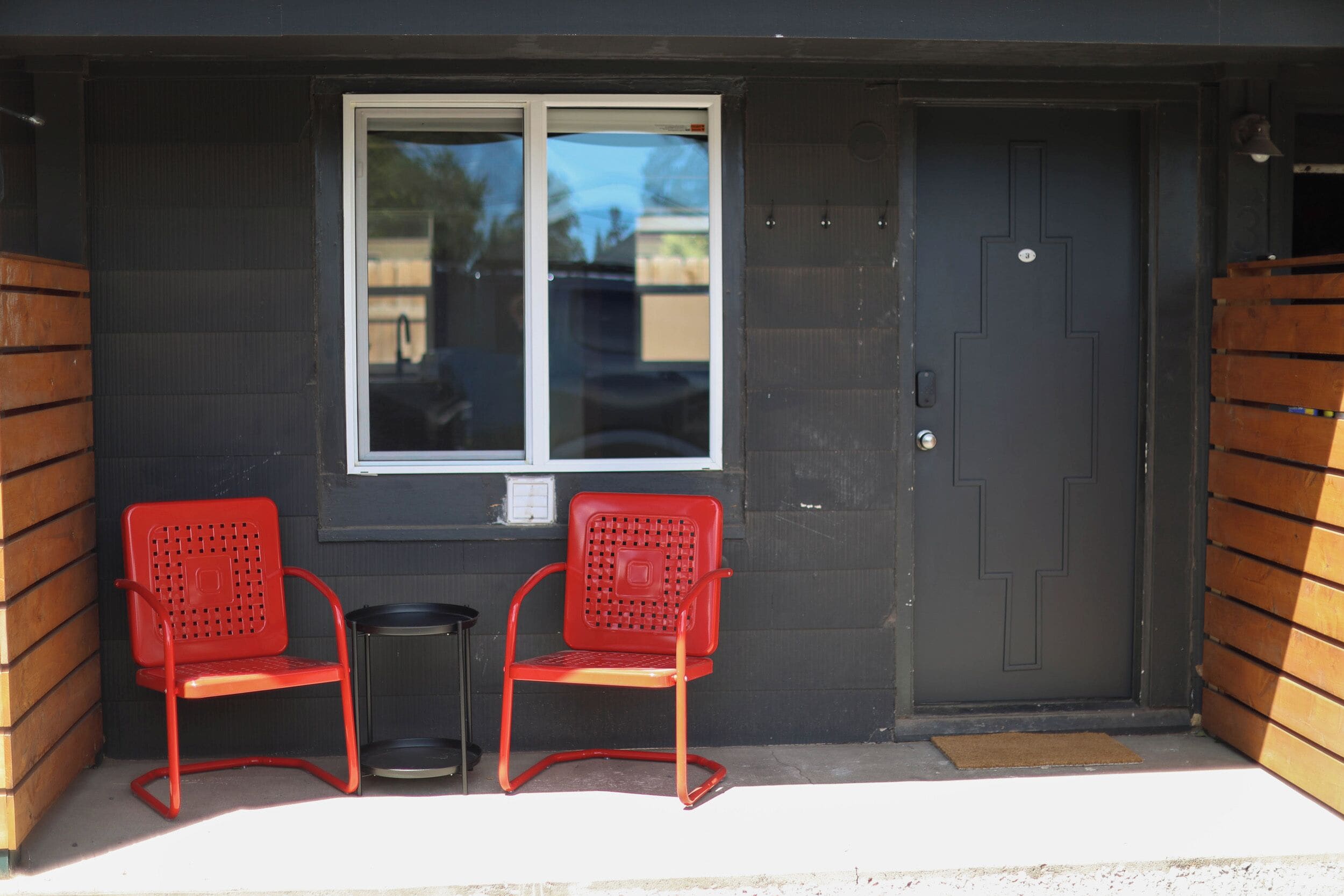 A building entrance with a dark door, a window, and two red chairs outside.