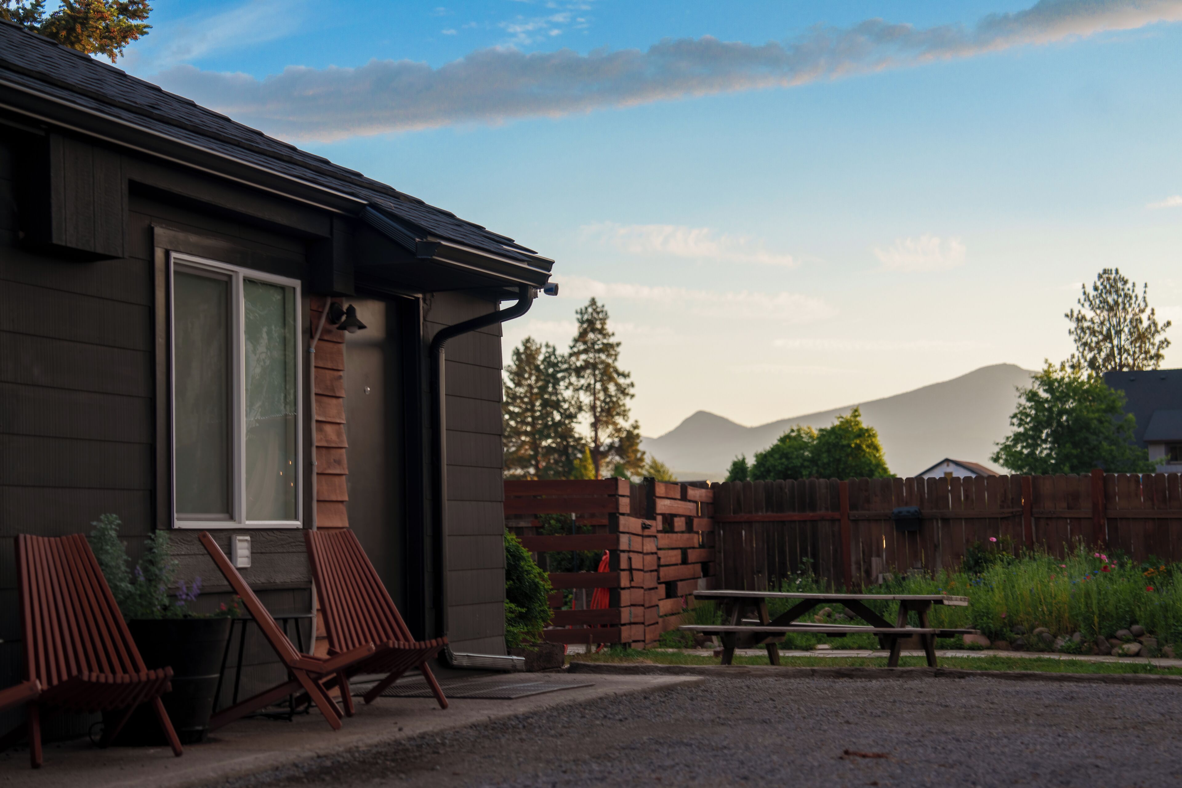 A house with a patio, two wooden chairs, a table, and a brick wall.