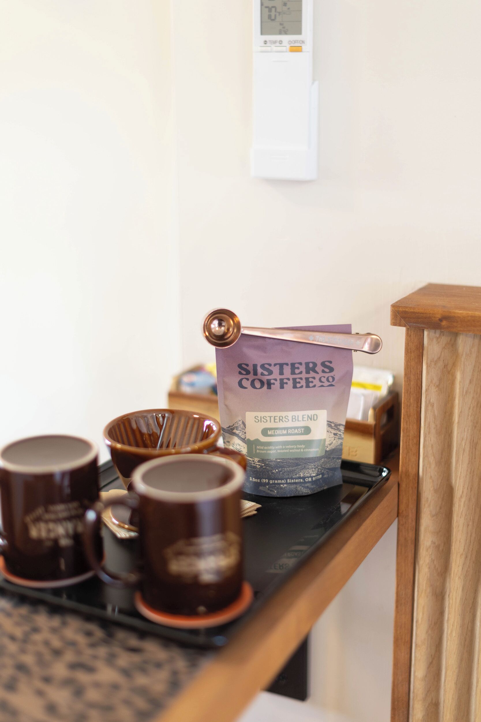 A coffee station with a bag of Sisters Blend coffee, a coffee machine, and several mugs on a tray.