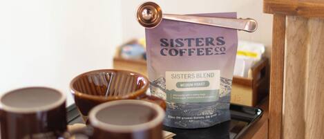 A coffee station with a bag of Sisters Blend coffee, a coffee machine, and several mugs on a tray.