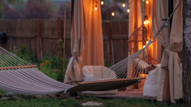 A hammock under a wooden pergola with string lights, a wooden fence, and a mountain in the background. - The Stranger Lodge (Sisters)