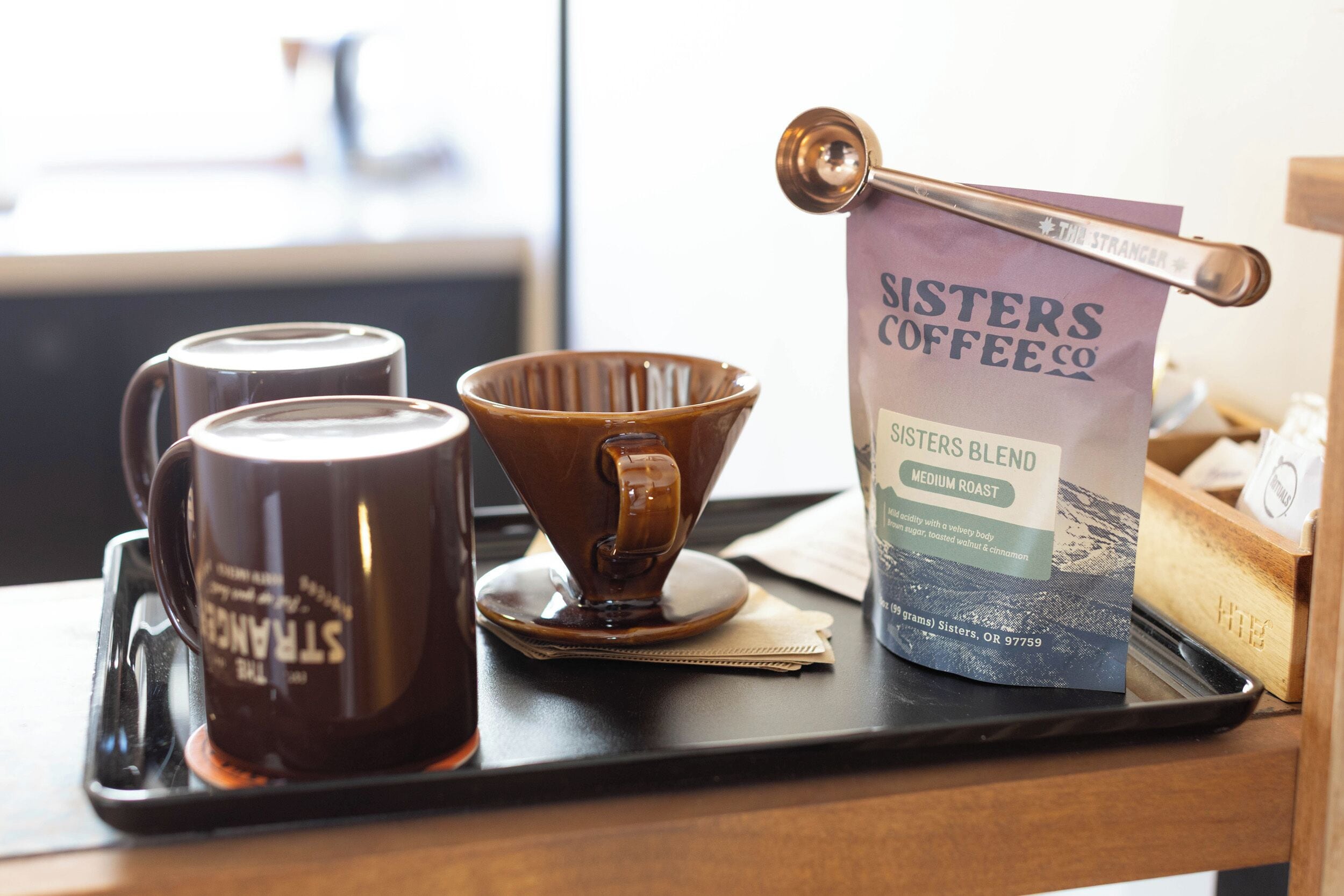 En bakke med to kaffekrus, en kaffebrygger og en pose Susters Coffee Co. blend.