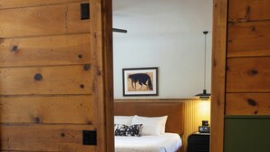 A wooden room with a bed, a nightstand, a lamp, and a framed picture on the wall. - The Stranger Lodge (Sisters)
