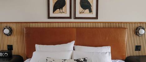 A hotel room with a bed, two framed bird paintings, a brown headboard, and a wall-mounted air conditioner.