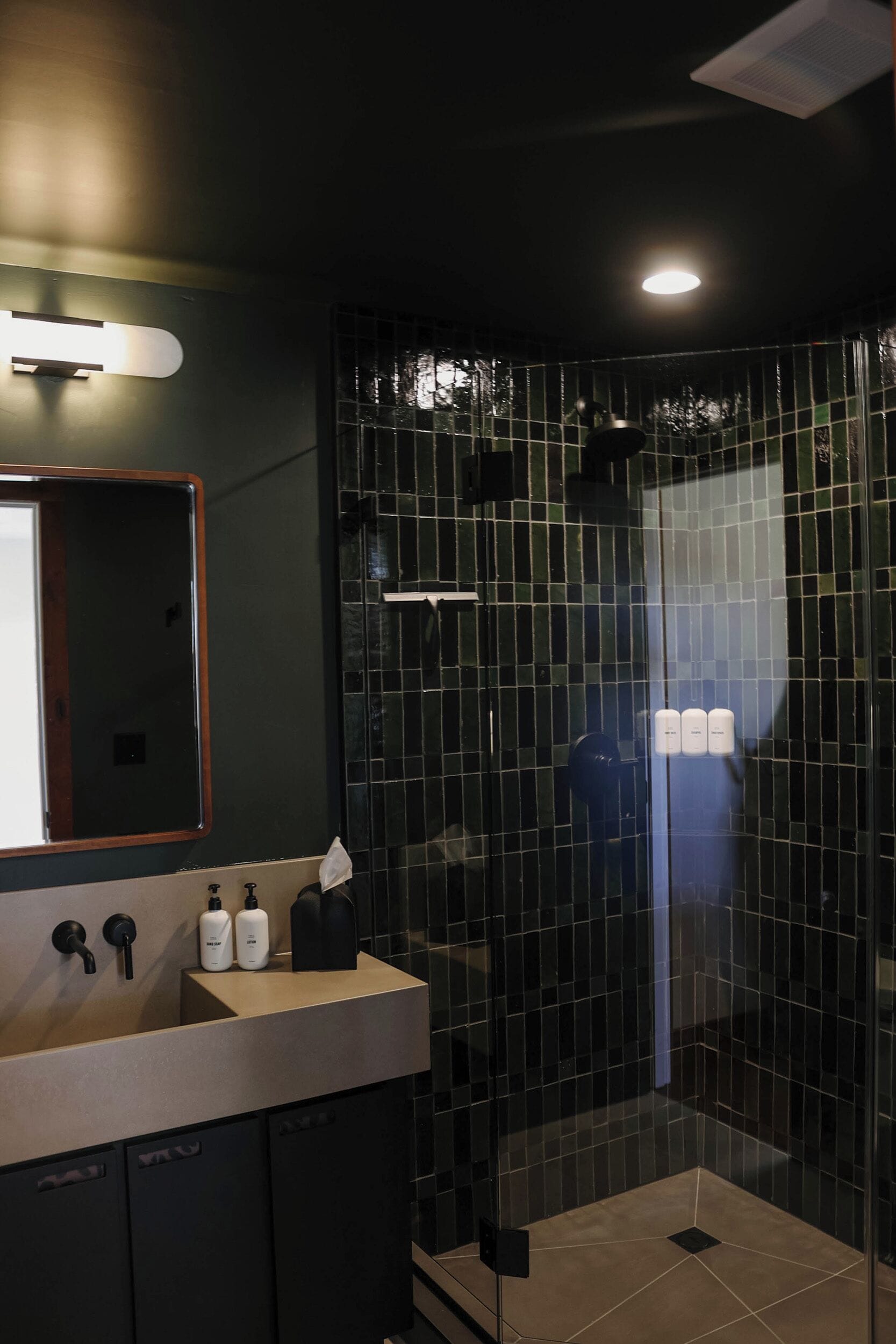 A modern bathroom with a glass shower enclosure, a sink with toiletries, and a mirror.