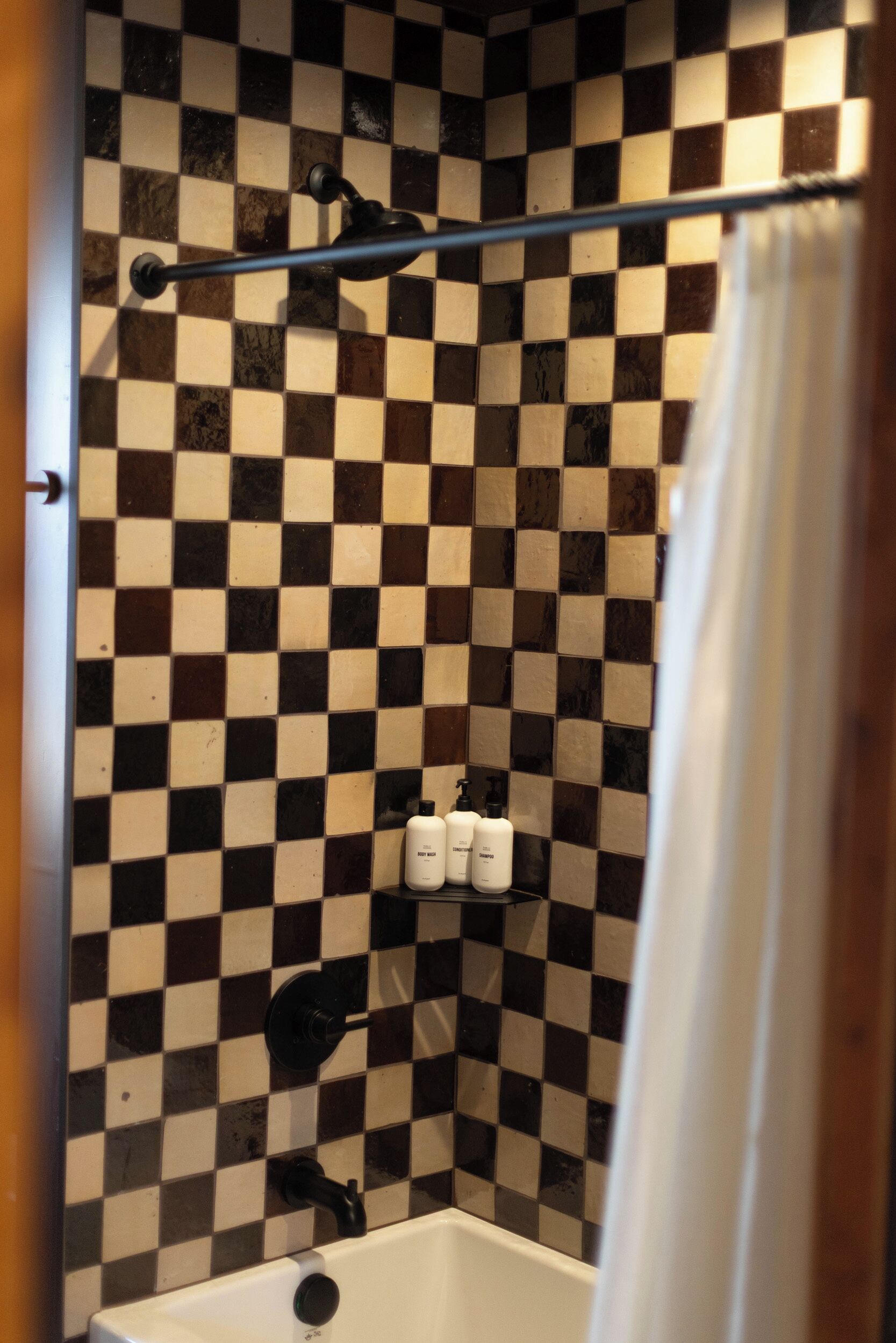 Un baño con pared de baldosas a cuadros, una cortina de ducha y una bañera.