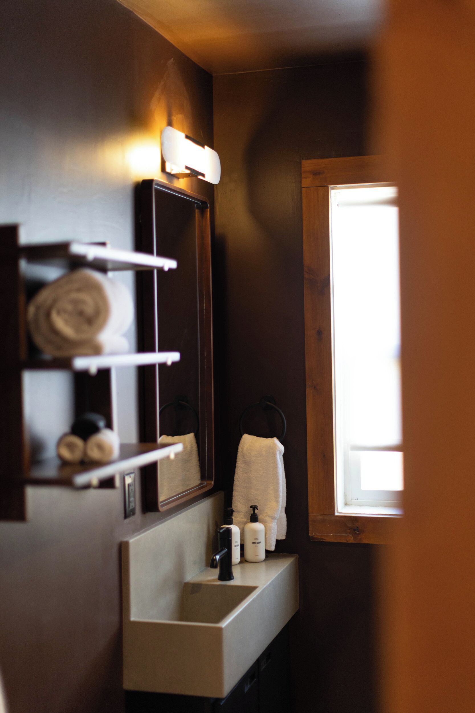 Une salle de bain avec un miroir, un porte-serviettes, un lavabo et une fenêtre.