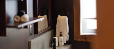 Une salle de bain avec un miroir, un porte-serviettes, un lavabo et une fenêtre.
