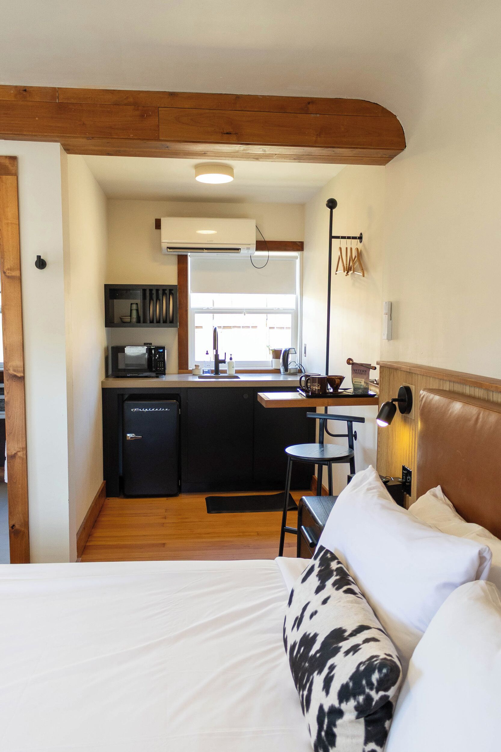 A compact room with a bed, a small kitchenette, and a wooden ceiling.