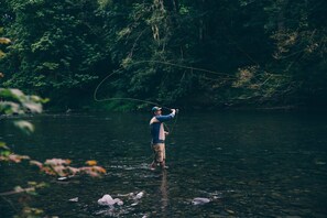 A person standing in a river surrounded by dense forest. - The Stranger Lodge (Sisters)