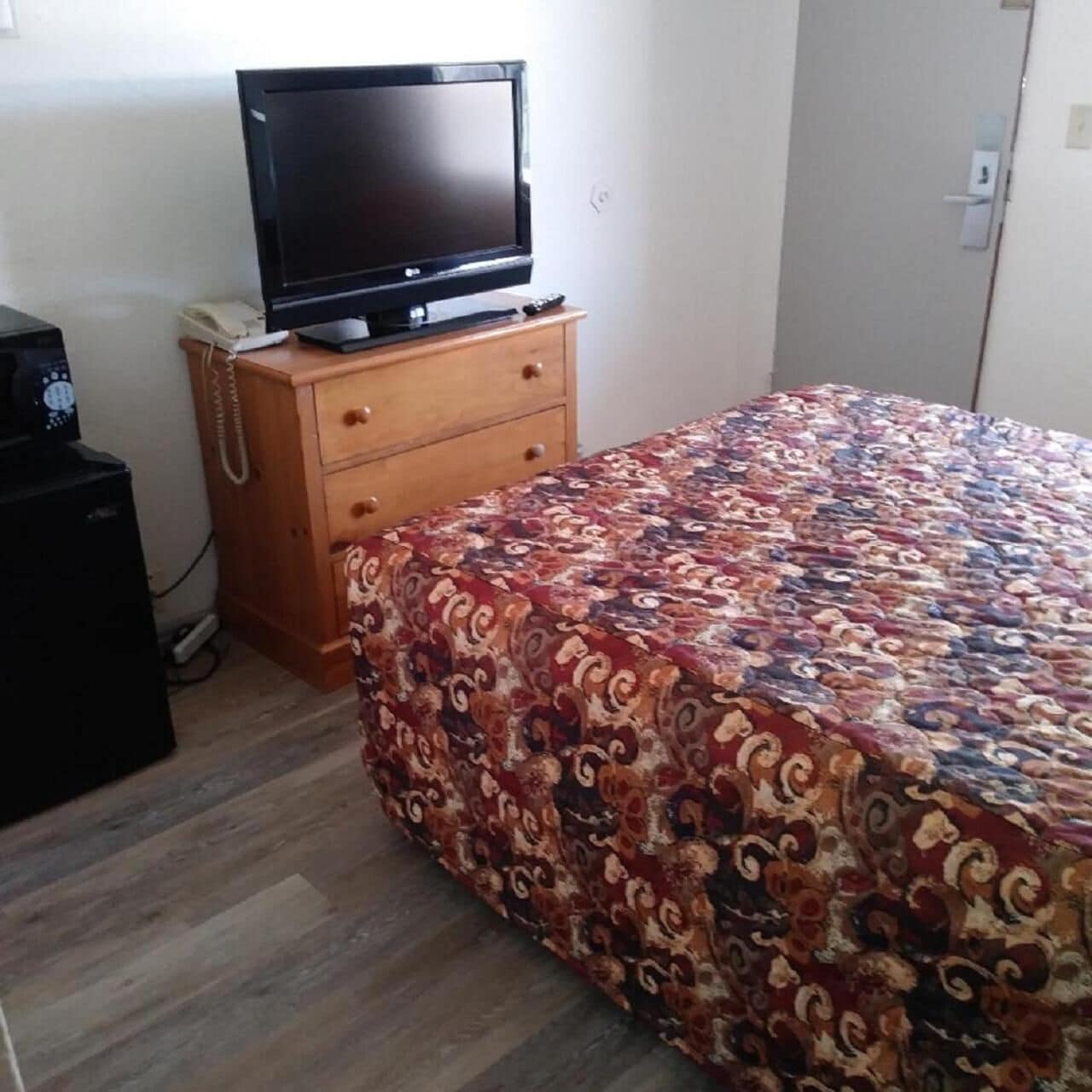 A bedroom with a bed, a television on a wooden dresser, and a small desk with a telephone.
