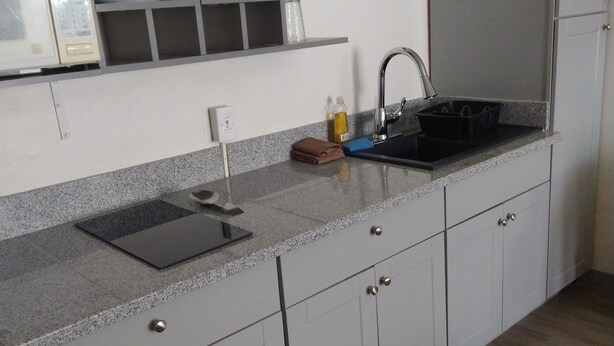A kitchen with a granite countertop, white cabinets, a built-in microwave, a sink with a faucet, and a wall-mounted air conditioner. - Budget INN (Durango)