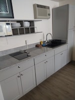 Una cocina con encimera de granito, armarios blancos, microondas integrado, un lavabo con grifo y un aire acondicionado instalado en la pared.