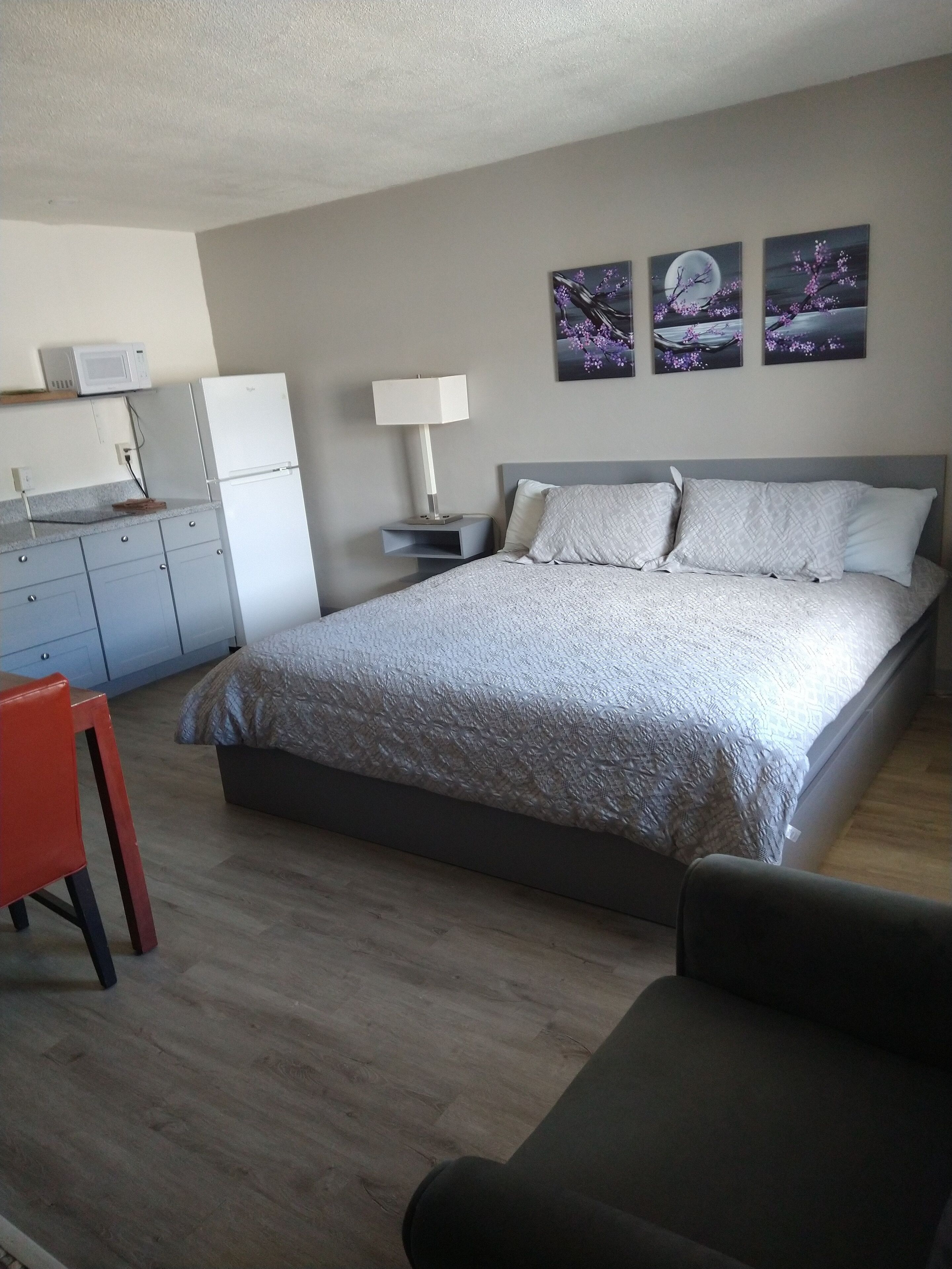 Camera da letto con un letto, comodini, una lampada, una piccola scrivania con una sedia e un forno a microonde sopra il bancone.